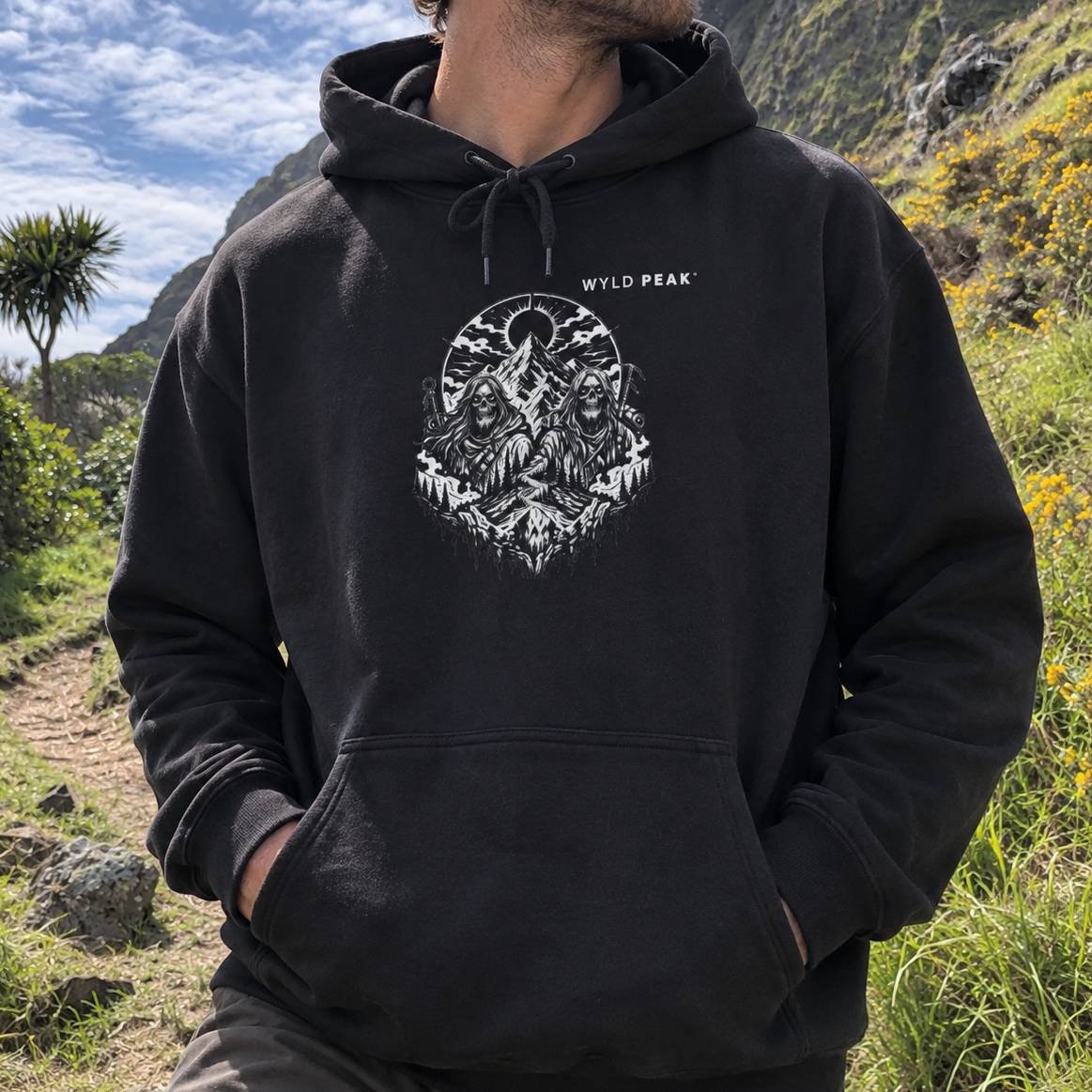 A man wearing a black pullover hoodie with a white graphic print of three figures in front of a mountain peak, set in an outdoor hiker's environment.