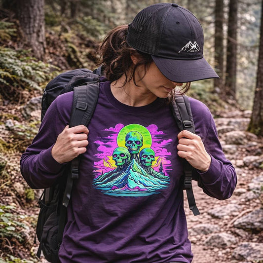 Person wearing a purple t-shirt with a colorful graphic design, holding backpacks in a forest setting.