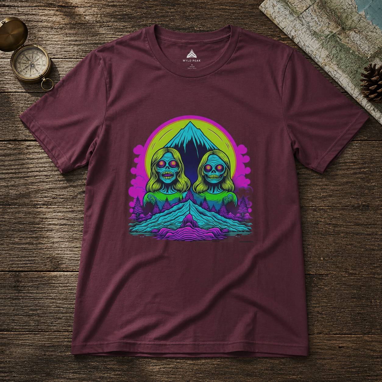 Maroon t-shirt with a colorful graphic design of two faces and a mountain on a wooden surface.