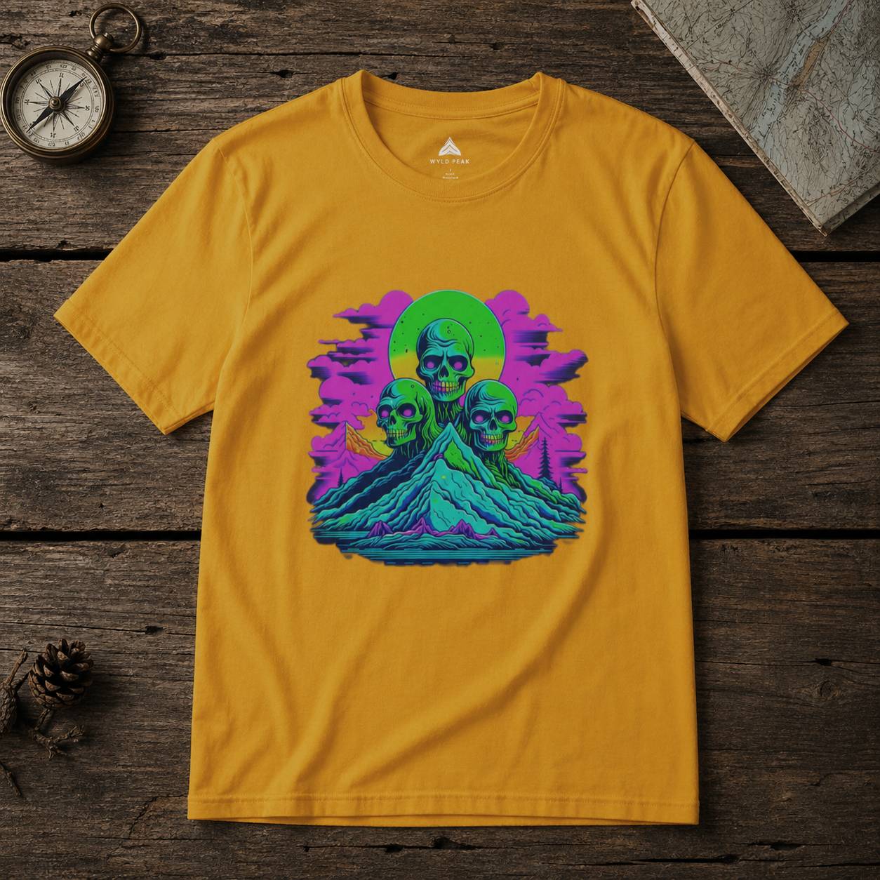 Yellow t-shirt with a colorful graphic design of skulls and nature elements on a wooden surface.