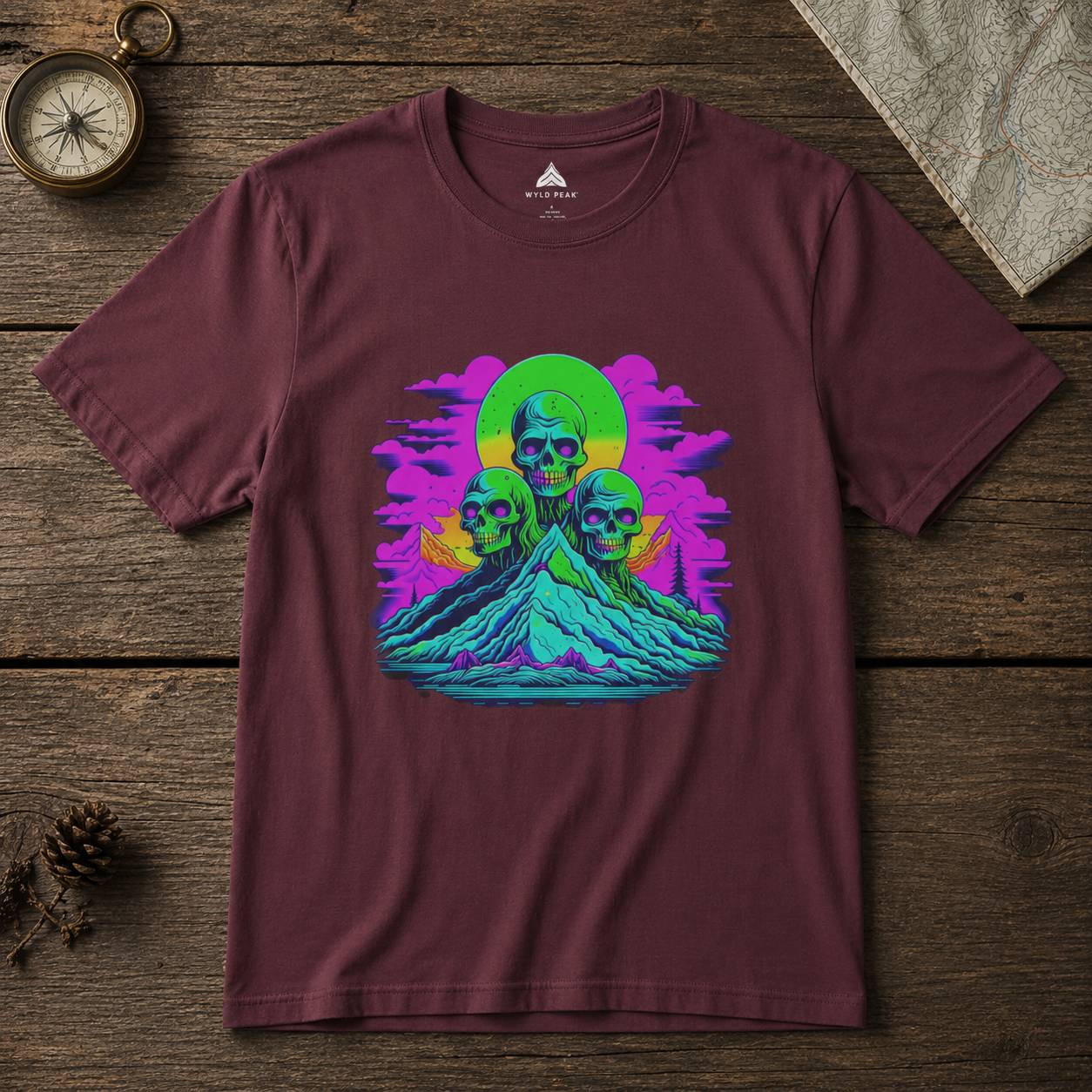 Maroon t-shirt with colorful graphic design of skulls and a rainbow circle on a wooden surface.