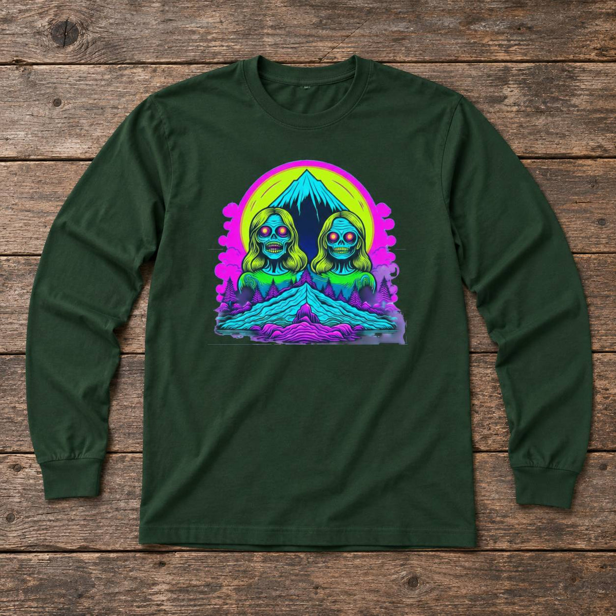 A dark green long-sleeve t-shirt with a colorful retro graphic of two alien-like figures in front of a mountain, laid flat on a rustic wooden plank background.