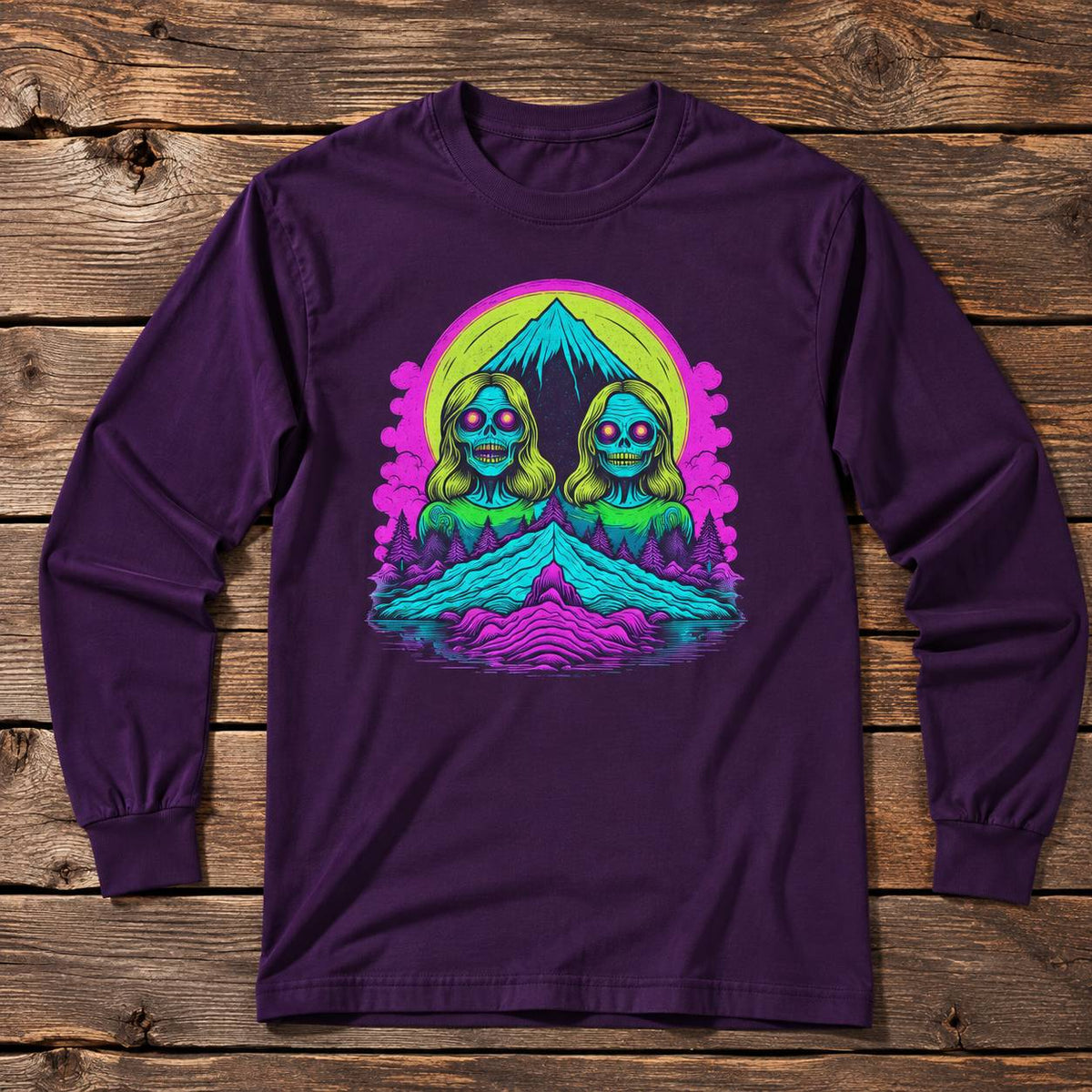 A dark purple long-sleeve t-shirt with a colorful retro graphic of two alien-like figures in front of a mountain, laid flat on a rustic wooden plank background.