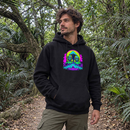 A man wearing a black pullover hoodie with a colorful psychedelic graphic of two skulls under a rainbow, standing on a forest path.