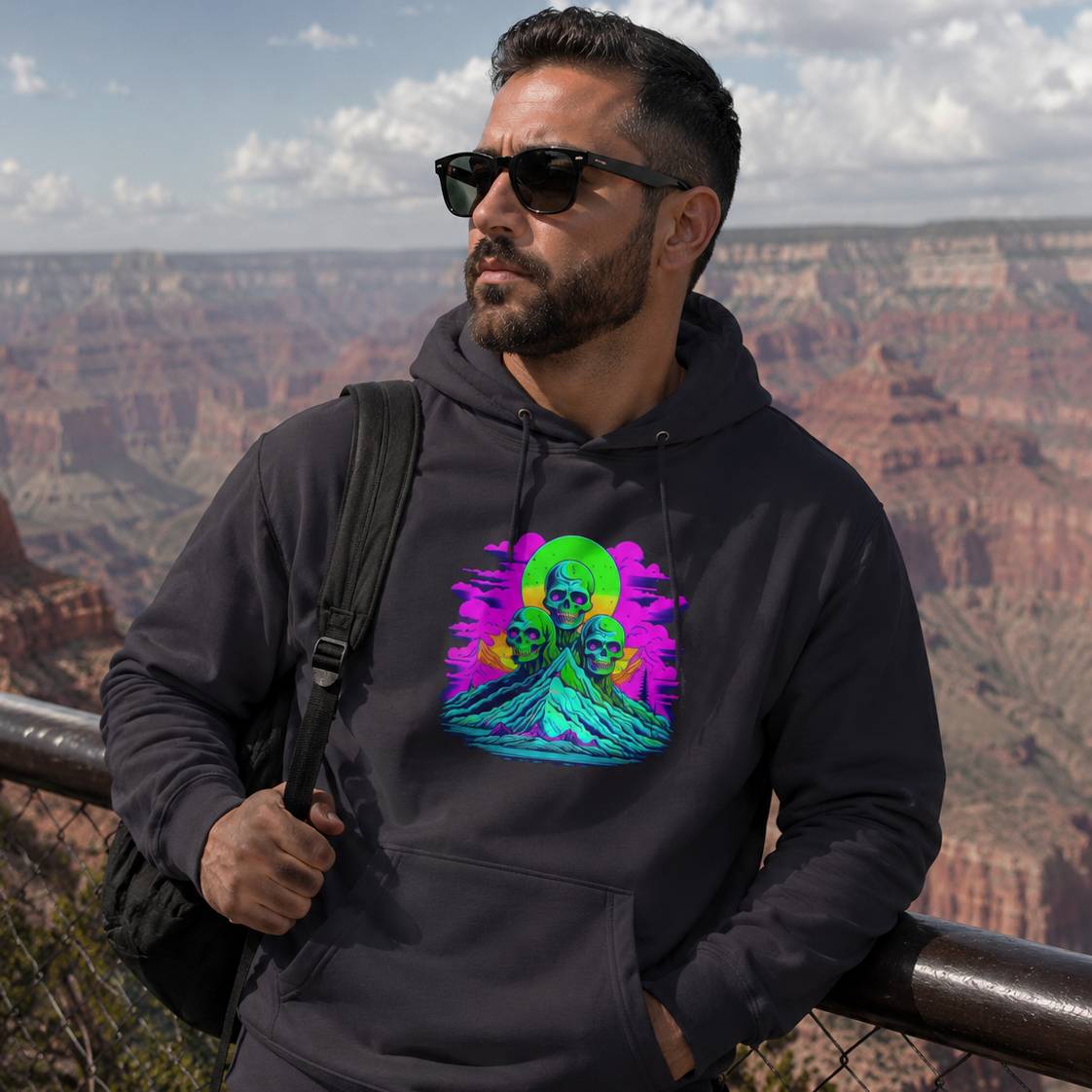 Man wearing a black hoodie with a colorful graphic design, standing in front of a scenic landscape.