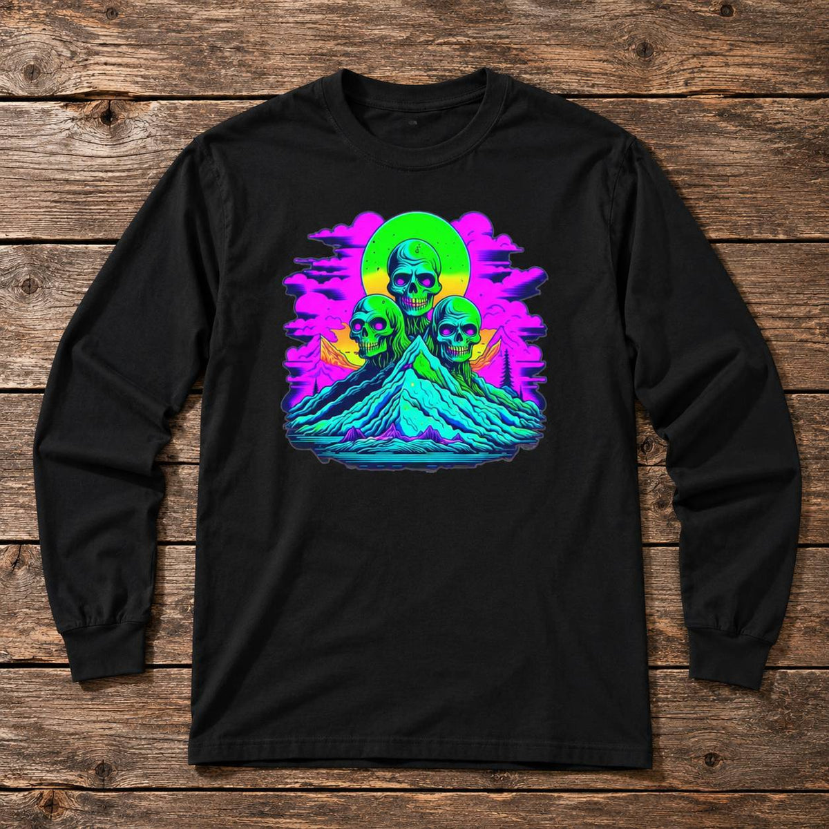 A black long-sleeve t-shirt with a colorful retro graphic of three skulls on a mountain under a neon sun, laid flat on a rustic wooden background.