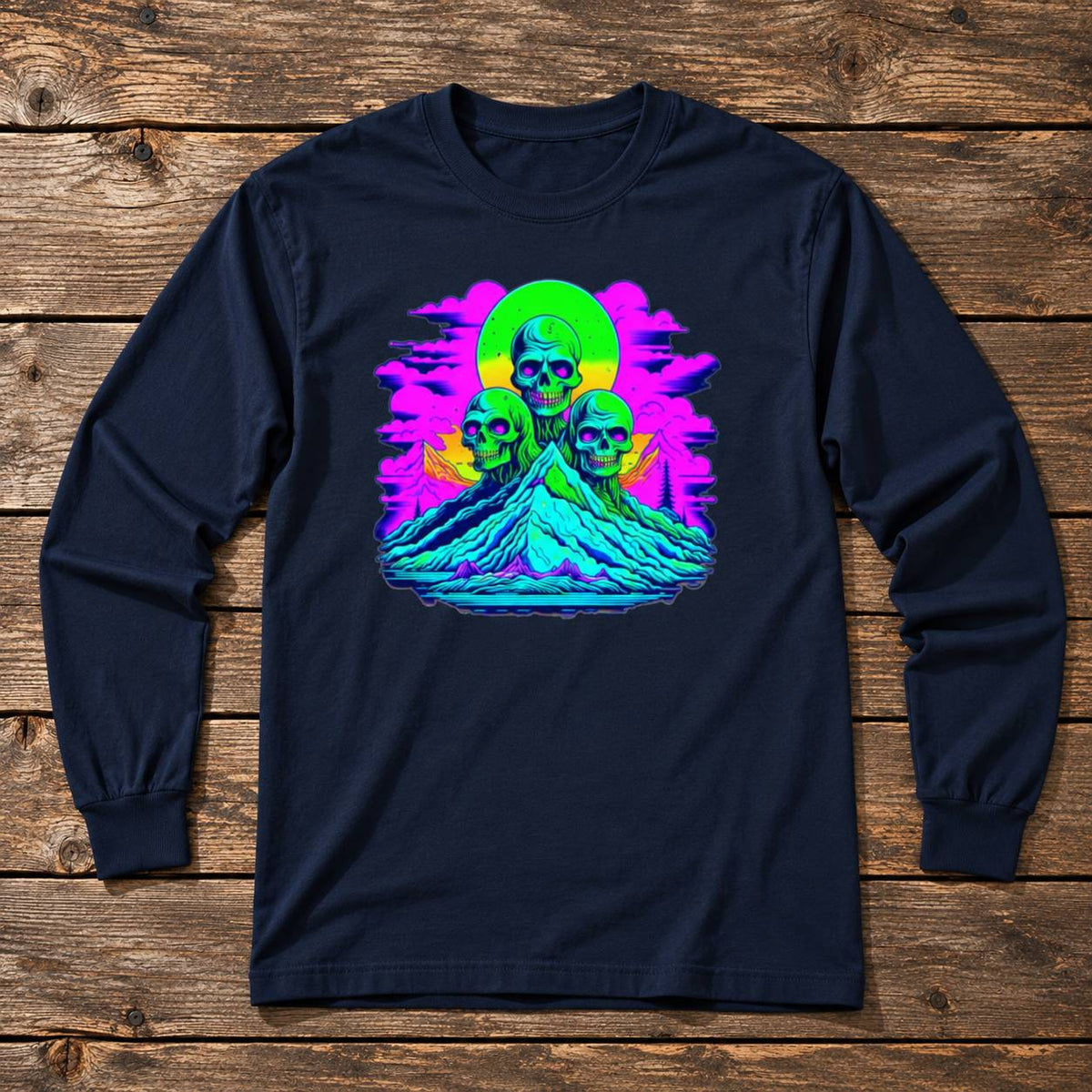 A navy blue long-sleeve t-shirt with a vibrant, colorful graphic print of three skulls on a mountain under a neon sun, displayed flat on a rustic wooden background.